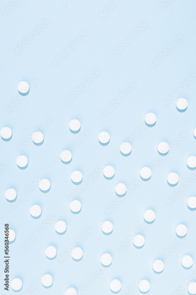 White tablets or pills pattern on soft light pastel blue color in hard light, top view, vertical, border, copy space. Pharmacy background in simple style, medical, remedies for teraphy disease.