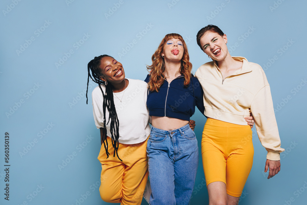 Cheerful female friends making funny faces while standing together in a studio