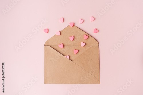 Small hearts fly out of a craft envelope on a pink background.