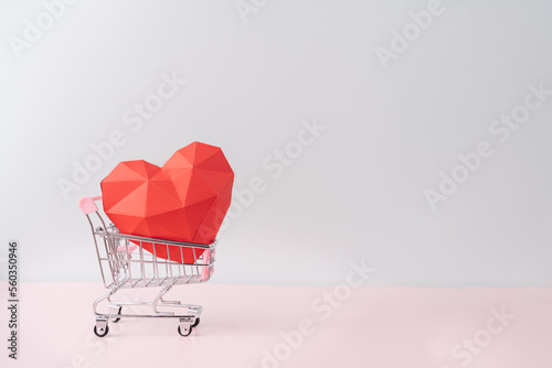 Fotografia, Obraz Red paper heart in a shopping cart against blue background.