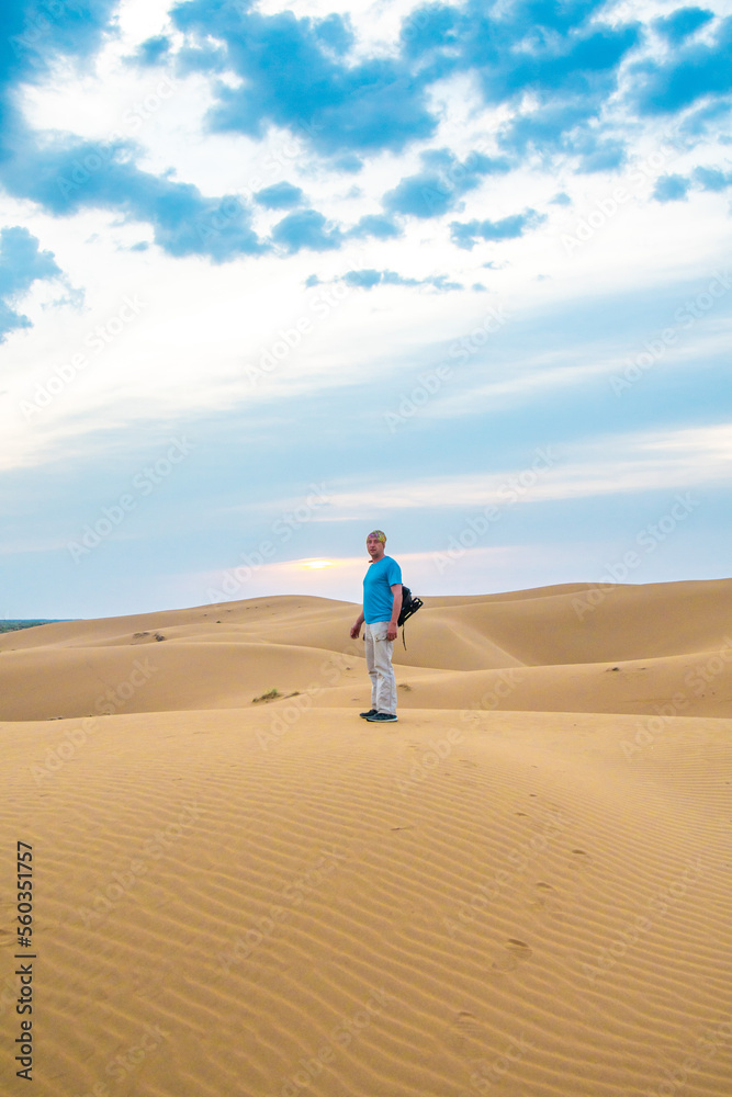 One man stands on a sand dune in the Kyzylkum desert at sunrise.