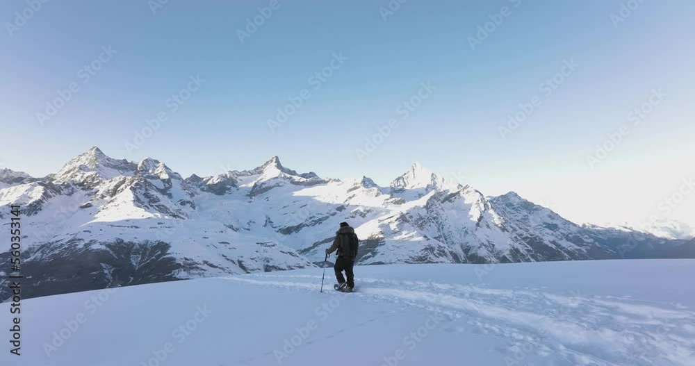 Aerial drone of Young man tourist hiker walking in snow shoes. Successful climber hiking up to mountain top swiss alps, Switzerland. Active travel lifestyle winter outdoor activities. Slow motion. Aerial drone of Young man tourist hiker walking in snow shoes. Successful climber hiking up to mountain top swiss alps, Switzerland. Active travel lifestyle winter outdoor activities. Slow motion.