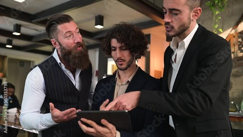 Group of three elegant guys using digital tablet and discussing about work and new ideas.