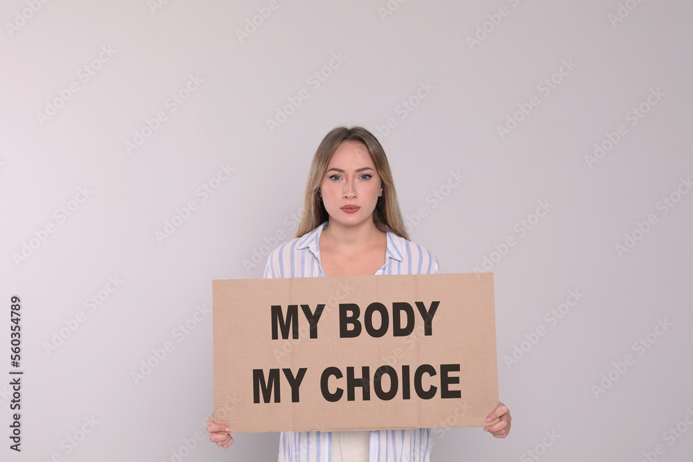 Woman holding placard with phrase My Body My Choice on light grey background. Abortion protest Woman holding placard with phrase My Body My Choice on light grey background. Abortion protest