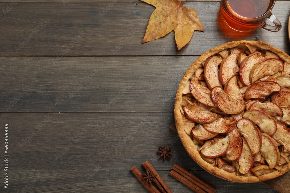 Delicious apple pie, cup of tea and cinnamon on wooden table, flat lay. Space for text