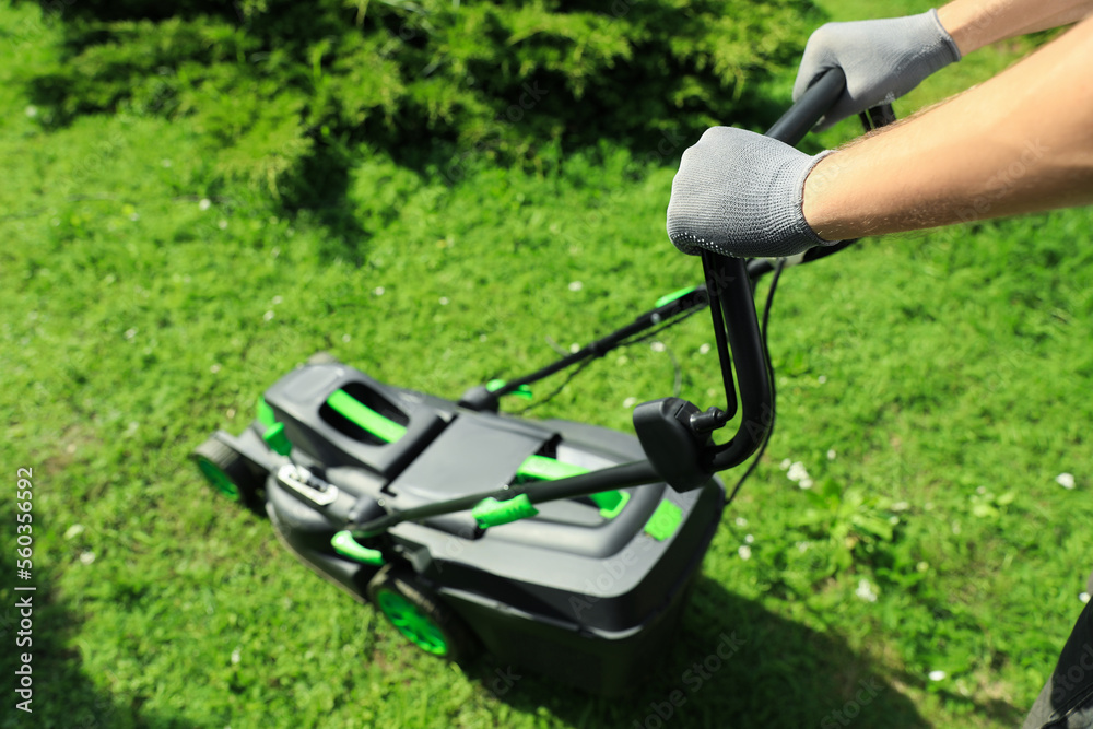 Man cutting grass with lawn mower in garden on sunny day, closeup Man cutting grass with lawn mower in garden on sunny day, closeup