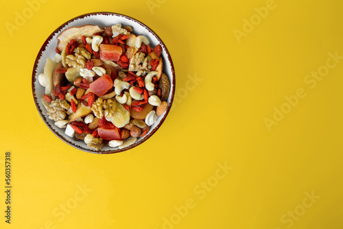 Fototapeta Naklejka Na Ścianę i Meble -  Bowl with mixed dried fruits and nuts on yellow background, top view. Space for text