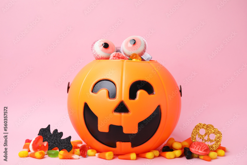 Fototapeta premium Halloween trick or treat bucket with different sweets on pink background