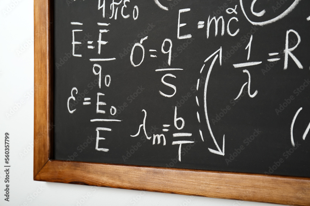 Blackboard with different physical formulas written with chalk on white wall Blackboard with different physical formulas written with chalk on white wall