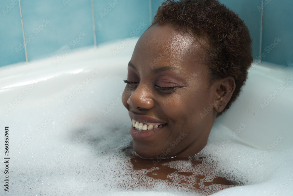 Portrait of African American woman, taking a bath with the bathtub full of foam, smiling happy and relaxed. Concept bath, relax, foam, soap.