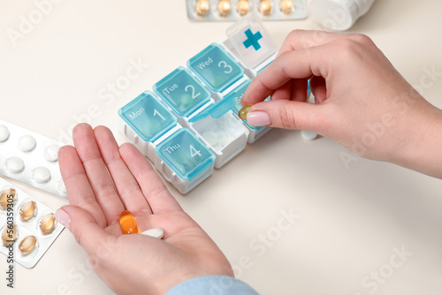 Woman taking pill from plastic container at white table, closeup