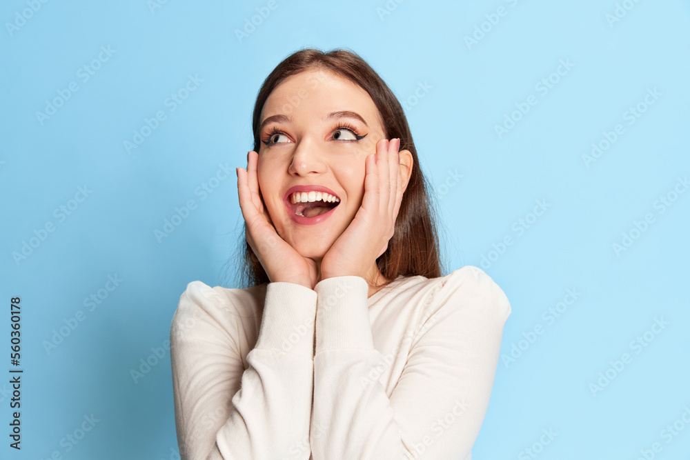 Happy and excited. Portrait of young, smiling, beautiful girl in casual clothes posing over blue studio background. Concept of emotions, lifestyle, youth Happy and excited. Portrait of young, smiling, beautiful girl in casual clothes posing over blue studio background. Concept of emotions, lifestyle, youth