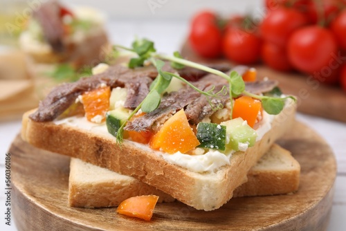 Delicious toasts with anchovies, cream cheese, bell peppers and cucumbers on white table, closeup