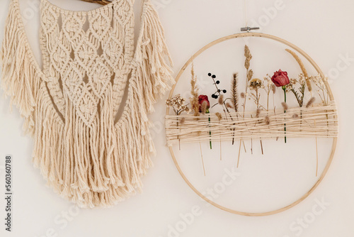 Stylish boho wreath with dry flowers and macrame hanging on white wall. Modern floral arrangement and creative handmade decor in modern boho room