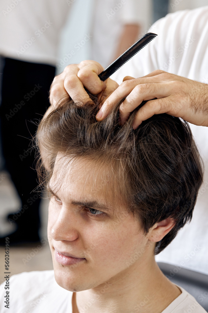 Fototapeta premium close-up, professional male hairstylist combing young customer's hair in barbershop