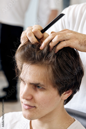close-up, professional male hairstylist combing young customer's hair in barbershop