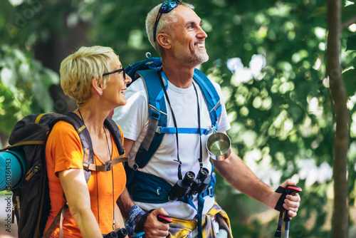 Fotografie Mature couple hiking in forest wearing backpacks and hiking poles