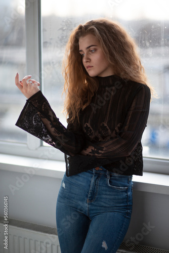 Free Download Beauty portrait of a beautiful young woman with curly hair, wear black suitcase and jeans, posing near bright windows. - GFXLoad