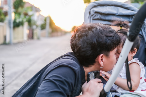 Asian father and daughter or son cute girl making kiss feeling happy and enjoy on baby stroller father and son eye contact smile so showing family love evening with sunlight on face happiness