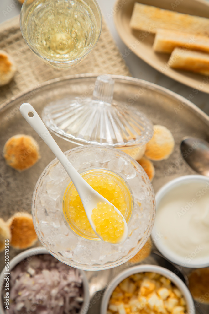 Gelber Saiblings Kaviar auf Eis in Glas Schale mit Porzellan Löffel, gekochte Eier Würfel, Charlotten Zwiebel Würfel, Toast Brot, Saure Sahne und Champagner Sekt auf Silber Teller und Marmor hell Gelber Saiblings Kaviar auf Eis in Glas Schale mit Porzellan Löffel, gekochte Eier Würfel, Charlotten Zwiebel Würfel, Toast Brot, Saure Sahne und Champagner Sekt auf Silber Teller und Marmor hell