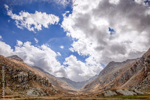 Sky with heavy low white clouds lying on peaks of Italian Alps, slopes are covered with autumn yellowed vegetation in gorge between mountains in Gran Paradiso National Park. Aosta Valley, Italy