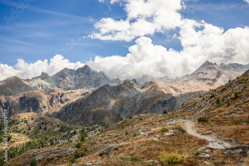 Alpine hiking path on granite slope covered with yellowed withered autumn grass and rare dwarf trees in Aosta Valley, Gran Paradiso National Park, Italy