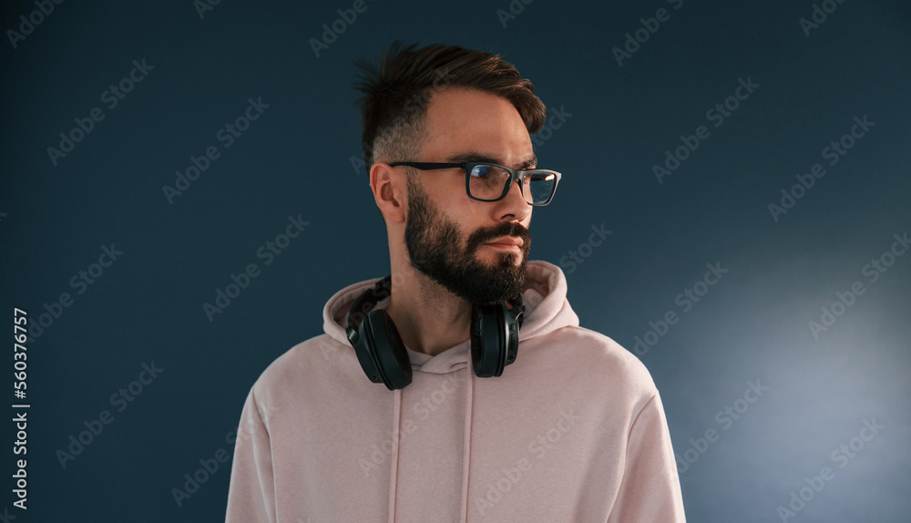 In glasses and with headphones. Handsome man is in the studio against blue background In glasses and with headphones. Handsome man is in the studio against blue background