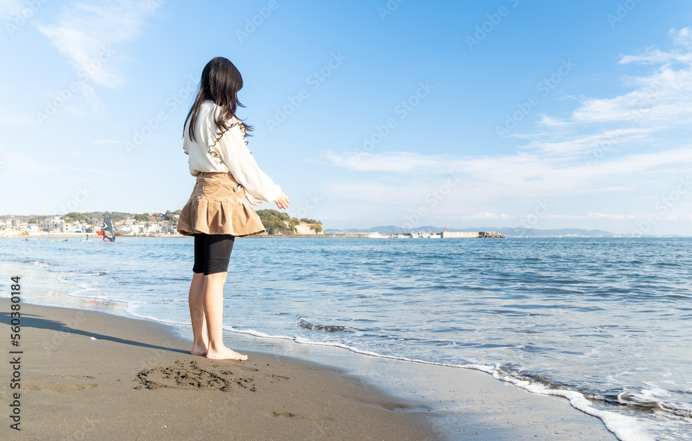 冬の海辺で海を見つめる10代の若い女性