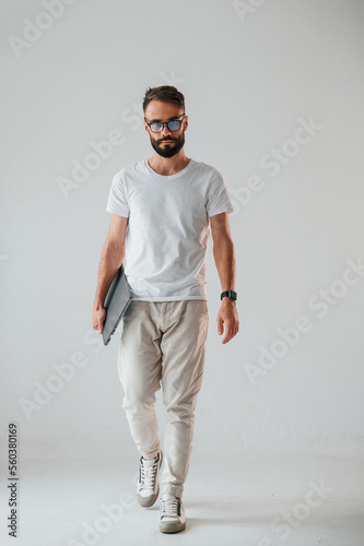 Front view. Holding laptop. Handsome man is in the studio against white background © standret