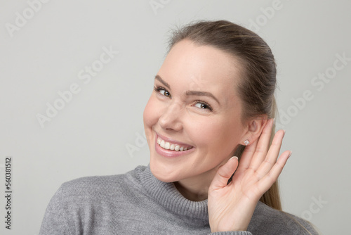Young smiling woman with hand at her ear tries to listen better  photo