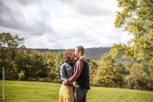 couple kissing with arms crossed in a field with mountains behind them photo