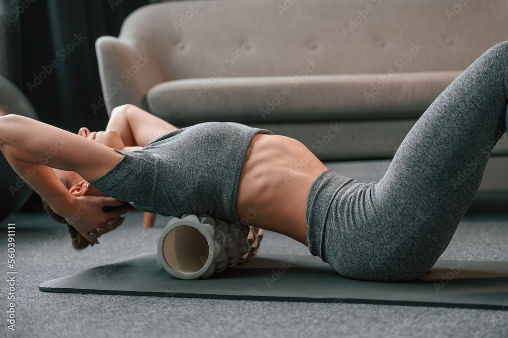 Foam roller for the spine. Young woman in yoga clothes doing fitness indoors