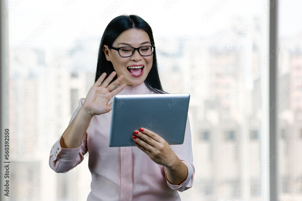 Fototapeta premium Young asian businesswoman to someone via tablet pc. Blurred windows backgorund.