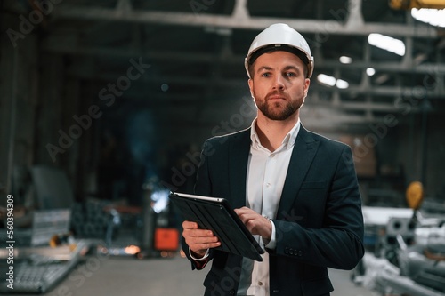 Holding black digital tablet in hands. Manager in black formal wear at the factory