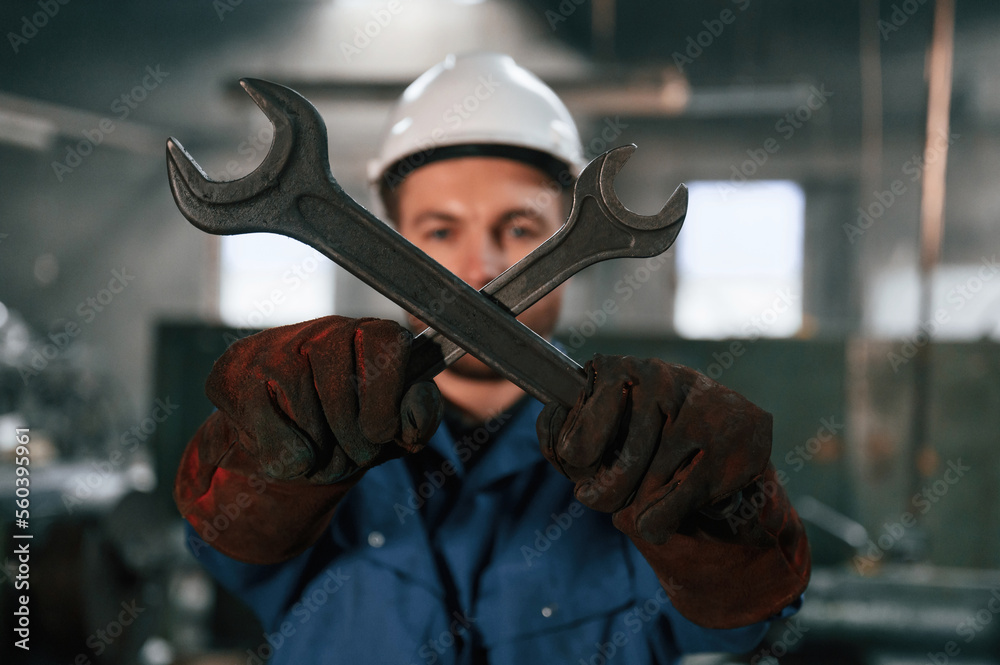 Holding two wrenches. Factory worker in blue uniform is indoors Holding two wrenches. Factory worker in blue uniform is indoors