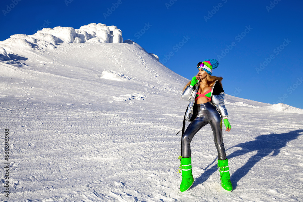 Sexy girl in a colorful bikini, winter hat and winter boots is posing in the mountains. Winter