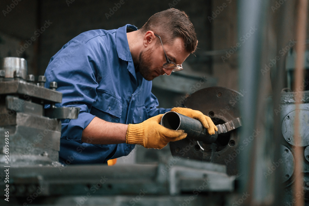 Busy by working with automatic machine. Man at factory and in blue uniform is indoors Busy by working with automatic machine. Man at factory and in blue uniform is indoors