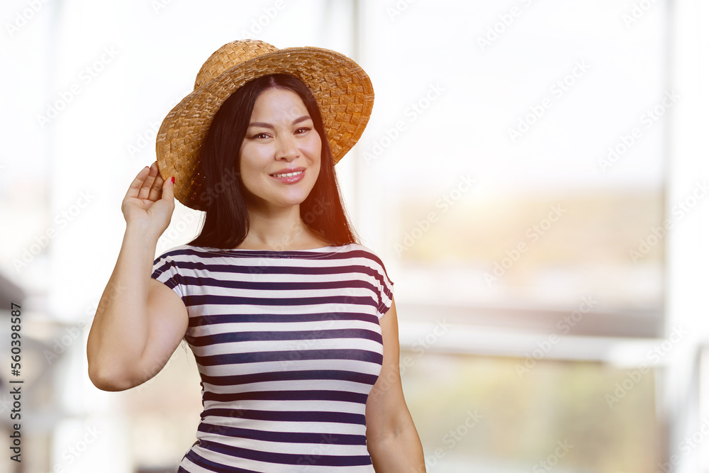 Happy young asian woman wearing straw hat indoors. Blurred windows background.