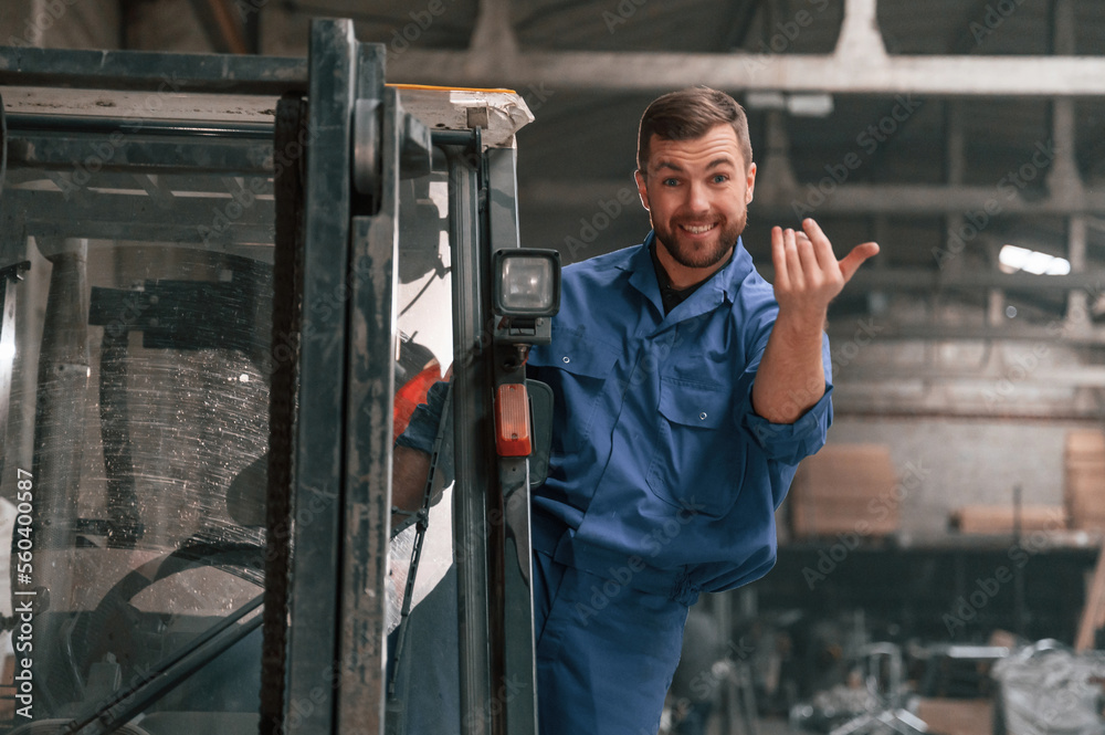 With the forklift. Factory worker in blue uniform is indoors With the forklift. Factory worker in blue uniform is indoors