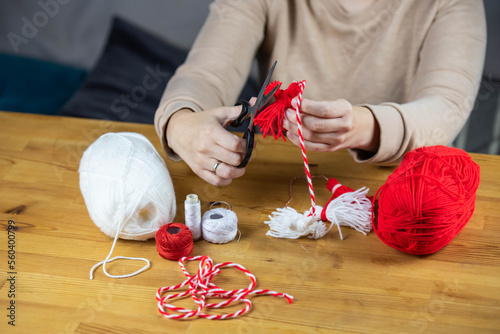 Woman making handmade traditional martisor, from red and white strings with tassel. Symbol of holiday 1 March, Martenitsa, Baba Marta, beginning of spring in Romania, Bulgaria, Moldova photo