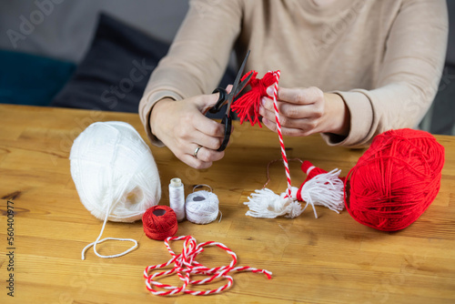 Woman making handmade traditional martisor, from red and white strings with tassel. Symbol of holiday 1 March, Martenitsa, Baba Marta, beginning of spring in Romania, Bulgaria, Moldova photo