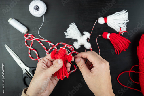 Woman making handmade traditional martisor, from red and white strings with tassel. Symbol of holiday 1 March, Martenitsa, Baba Marta, beginning of spring in Romania, Bulgaria, Moldova photo