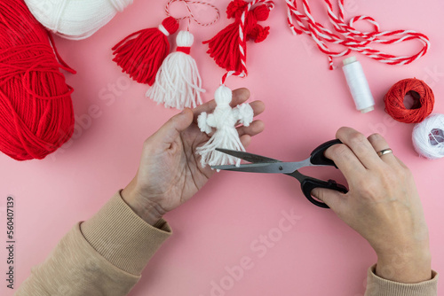 Woman making handmade traditional martisor, from red and white strings with tassel. Symbol of holiday 1 March, Martenitsa, Baba Marta, beginning of spring in Romania, Bulgaria, Moldova photo