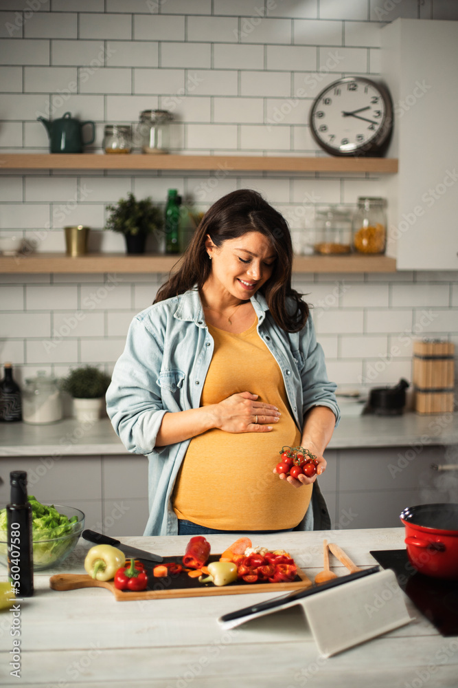 Young woman in kitchen. Beautiful pregnant woman making salad.