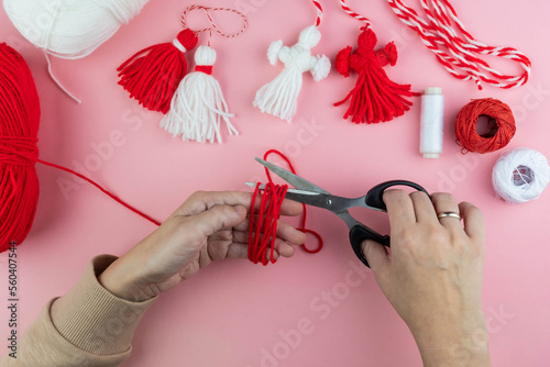 Woman making handmade traditional martisor, from red and white strings with tassel. Symbol of holiday 1 March, Martenitsa, Baba Marta, beginning of spring in Romania, Bulgaria, Moldova photo