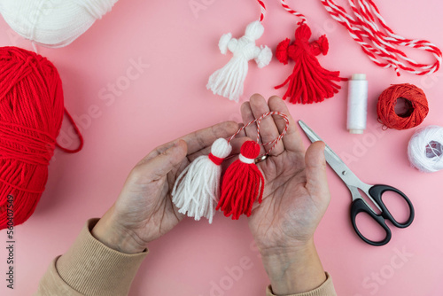 Woman making handmade traditional martisor, from red and white strings with tassel. Symbol of holiday 1 March, Martenitsa, Baba Marta, beginning of spring in Romania, Bulgaria, Moldova photo