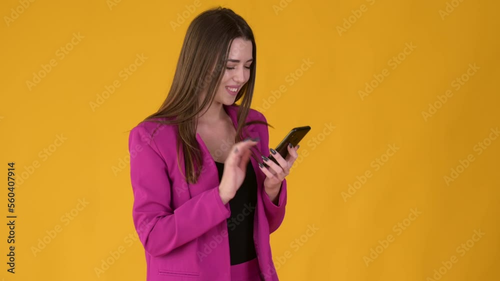 Young joyful girl using smart phone and texting online chat isolated on yellow background. People lifestyle concept. Young joyful girl using smart phone and texting online chat isolated on yellow background. People lifestyle concept.