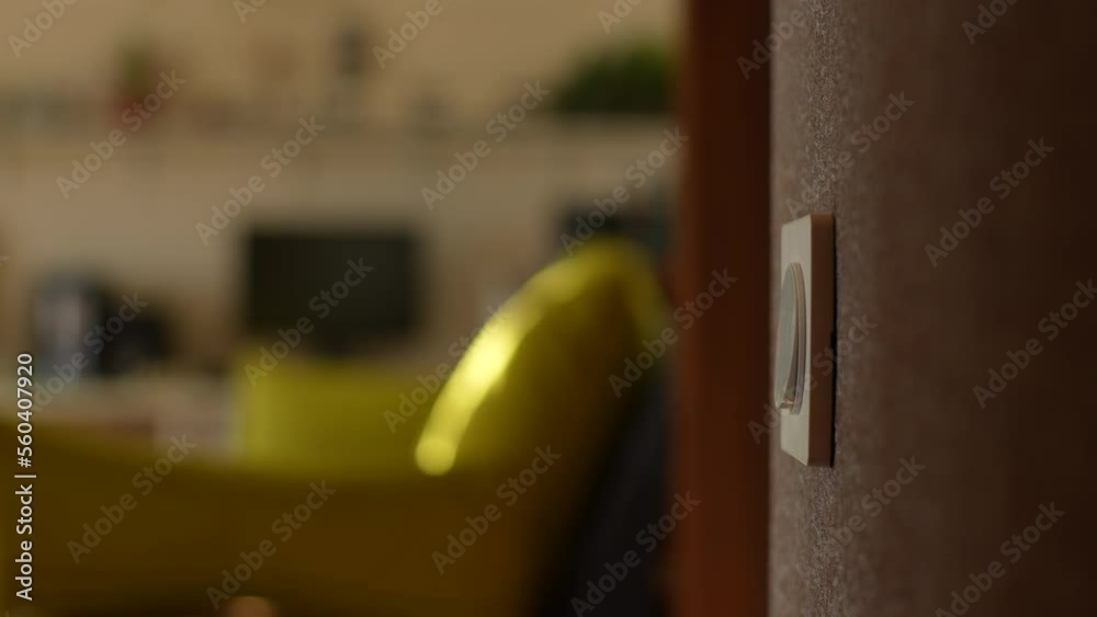 Close-up hands of unrecognizable young man turning light on and off by pushing switch on wall in dark bathroom, view of bright living room. Concept of home comfort. Shooting in slow motion.