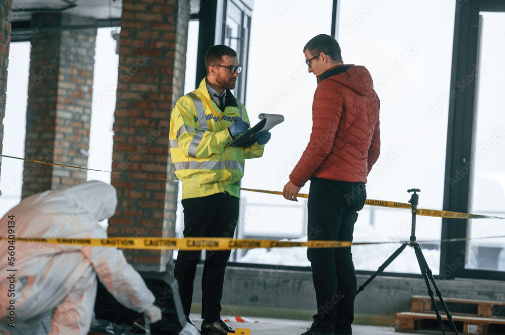 The witness is being questioned. Two detectives are collecting evidence in a crime scene The witness is being questioned. Two detectives are collecting evidence in a crime scene