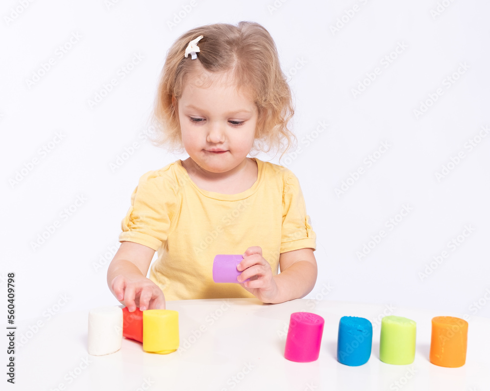 Cute little girl chooses colourful plasticine for modeling on a white background Cute little girl chooses colourful plasticine for modeling on a white background